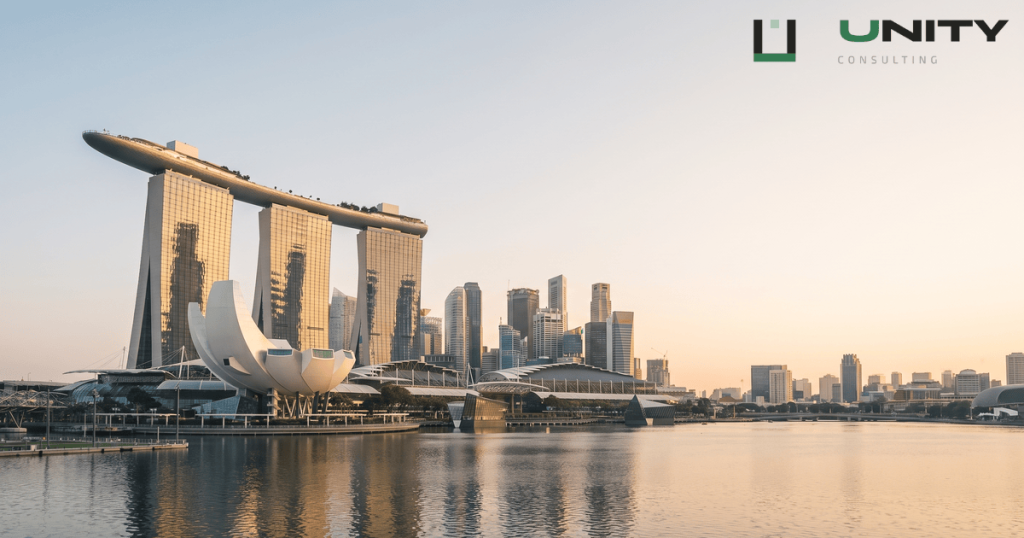 A wide, sunlit panorama of Singapore's Marina Bay financial district at sunrise, featuring the Marina Bay Sands hotel.