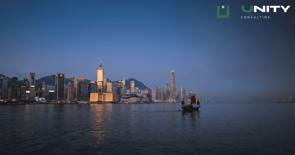 A blue-hour wide shot of Hong Kong's Victoria Harbour with the illuminated financial district skyline and dark water.
