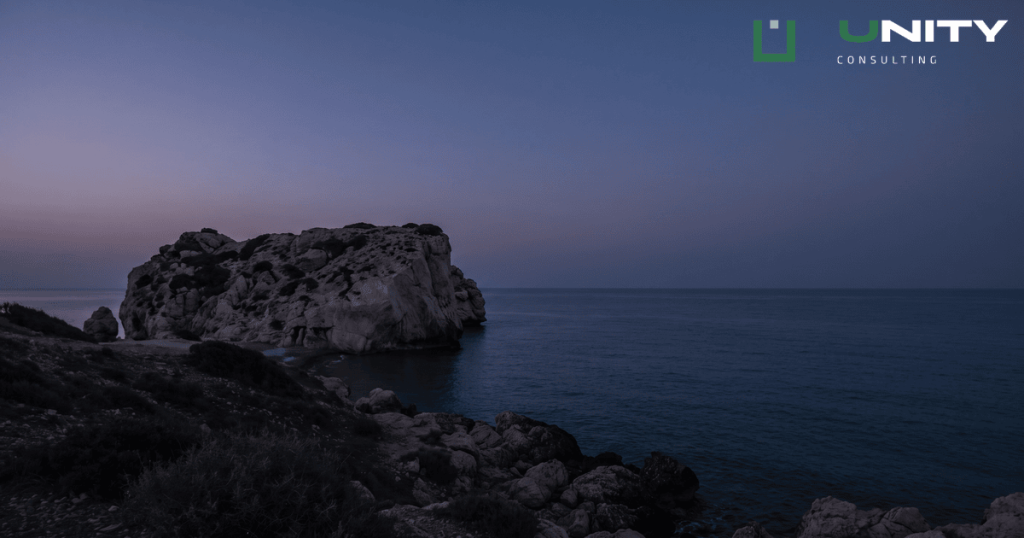 A wide shot of Aphrodite's Rock in Cyprus at blue hour, with the sea and sky in deep blue tones.