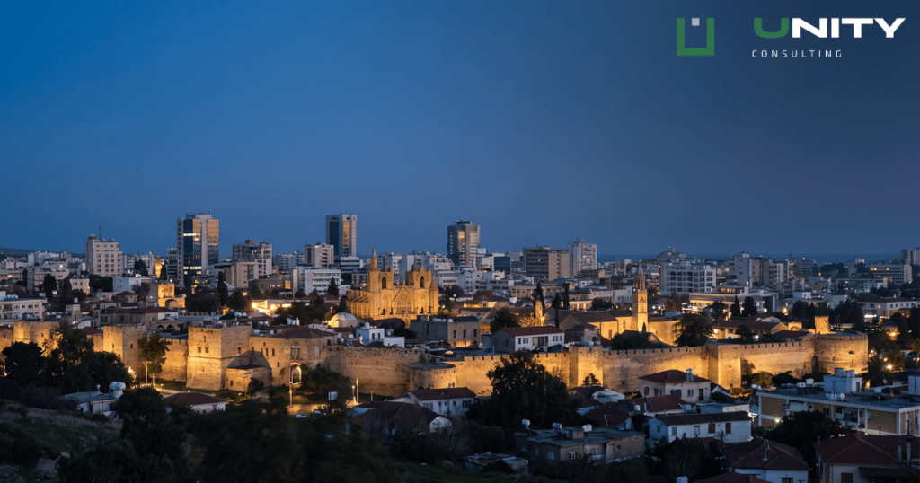 An elevated twilight view of Nicosia, Cyprus, showing city lights illuminating historic and modern buildings under a deep blue sky.