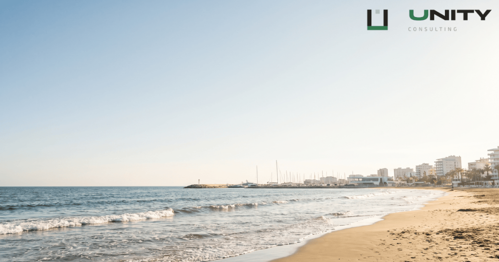 A sun-drenched wide-angle view of the Limassol coastline in Cyprus, with a sandy beach and marina under a clear blue sky.