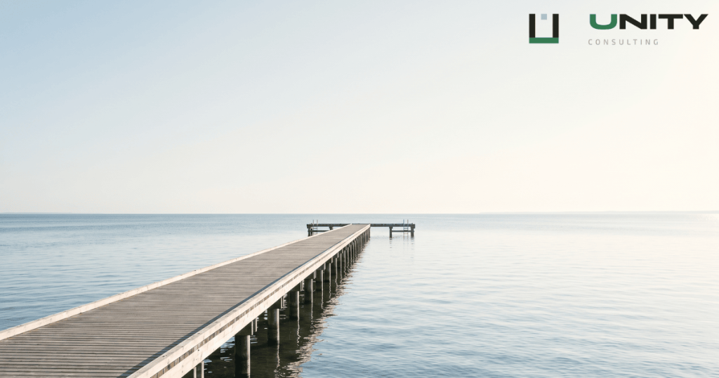 A long wooden pier stretches into the calm, pale blue Baltic Sea under a bright, open sky in Pärnu, Estonia.