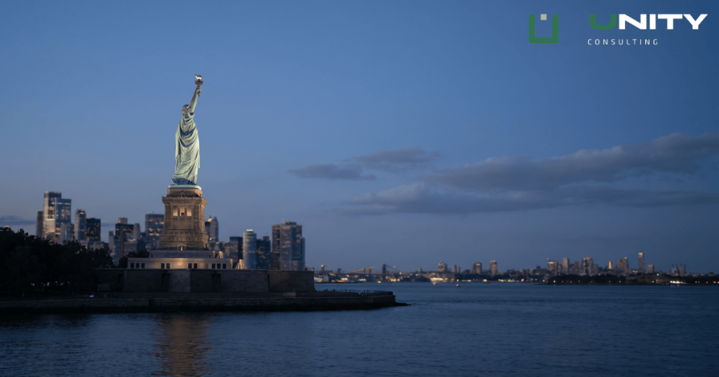 The Statue of Liberty stands illuminated against a dark blue twilight sky with calm harbour water in the foreground.