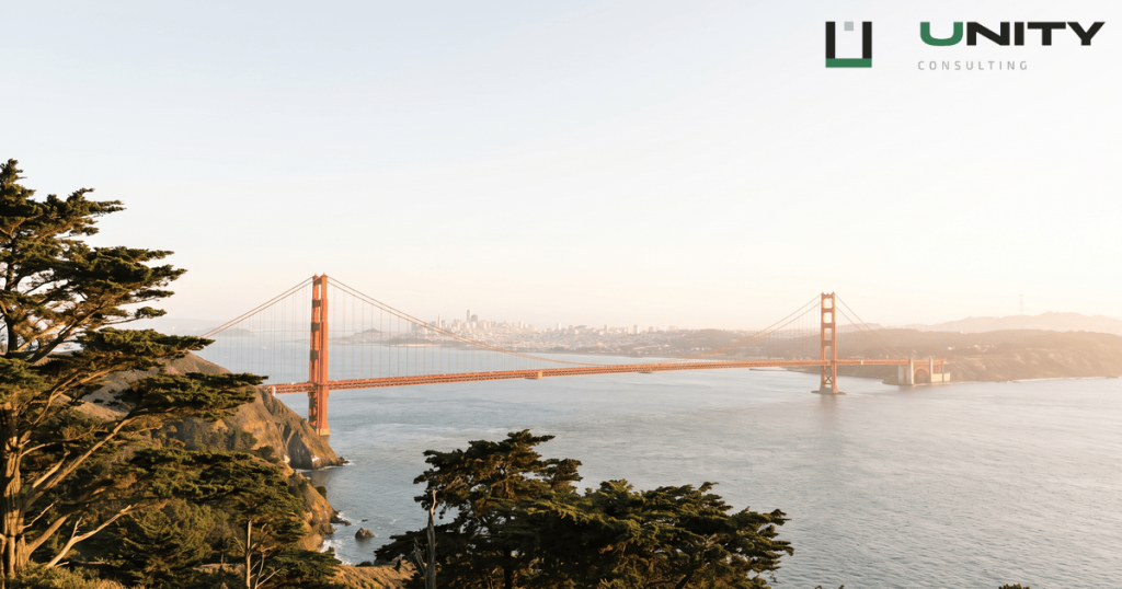 A wide shot of the Golden Gate Bridge under a bright sky, with San Francisco visible in the distance.