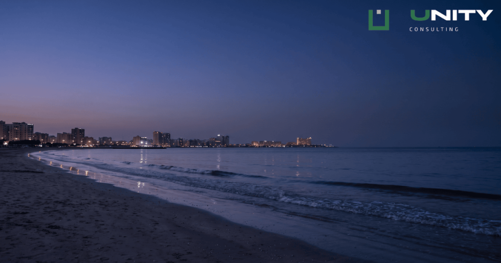 A wide view of the Ras Al Khaimah coastline at blue hour, with city lights reflecting faintly on the calm water.