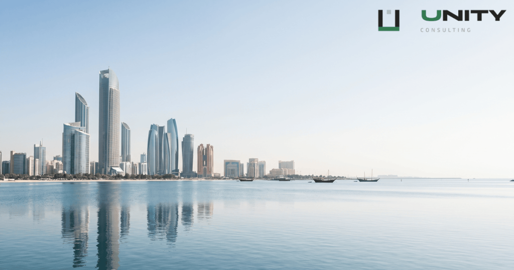 A wide, sunlit shot of the modern Abu Dhabi skyline reflected in the calm waters of the Arabian Gulf.