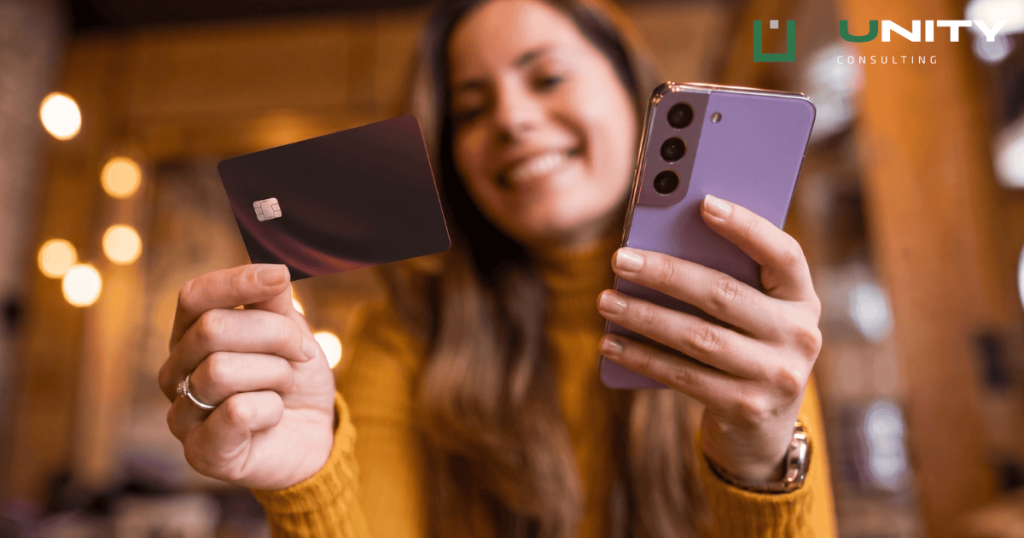 A woman holding a credit card and a smartphone, illustrating online card payments affected by Visa VAMP and VIRP rules